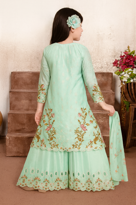 Woman wearing a light green embroidered outfit with a floral headband, standing against a neutral background.