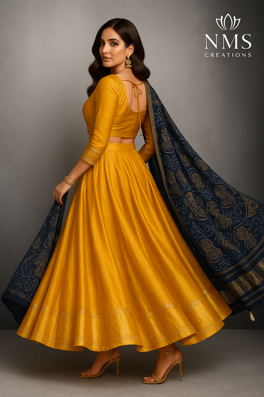 Woman wearing a yellow traditional outfit with a blue dupatta, branded 'NMS Creations'.