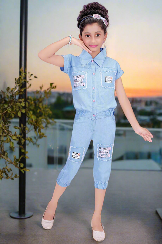 A girl wearing a light blue denim co-ord set with a short-sleeve button-up top and matching capri pants, featuring patchwork details.