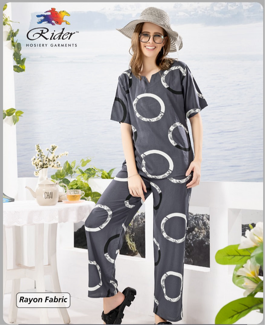 Woman in sunglasses and hat wearing grey printed rayon lounge set, standing outdoors with plants