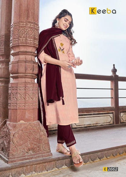 Woman in pink and maroon embroidered salwar suit with dupatta, standing in traditional architectural setting