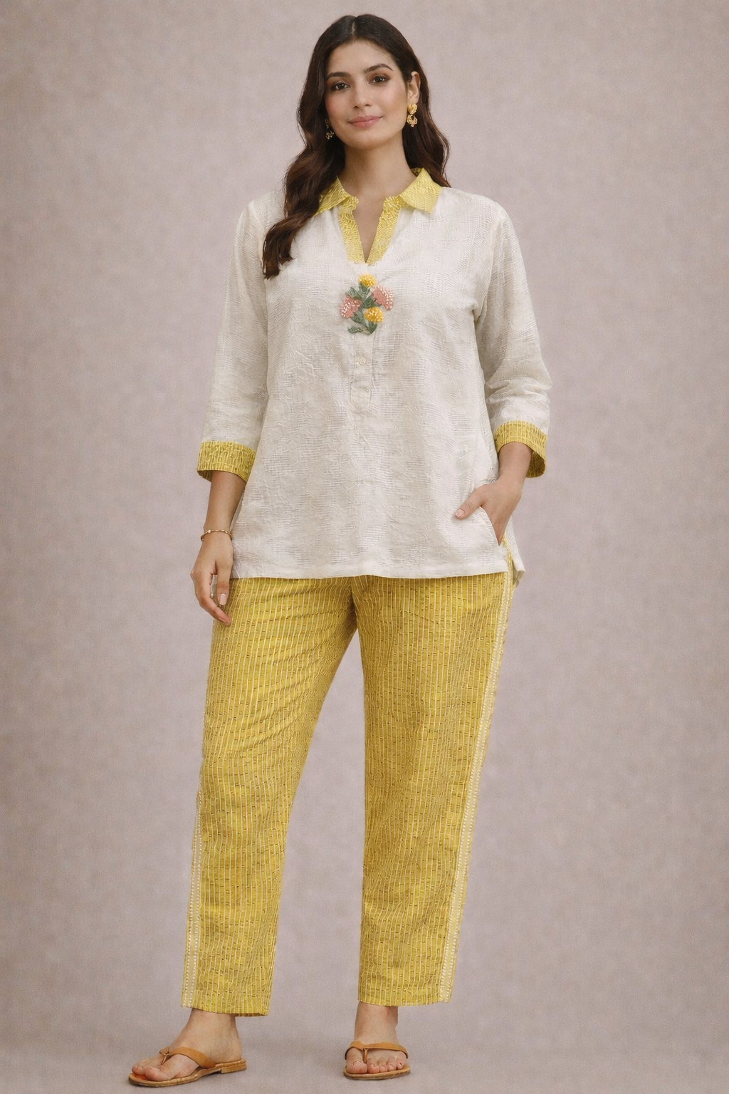 Woman wearing a white top with yellow accents and yellow pants on a plain background