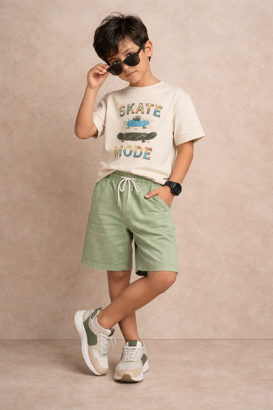Stylish boy in sunglasses wearing a skate graphic tee, green shorts, and sneakers