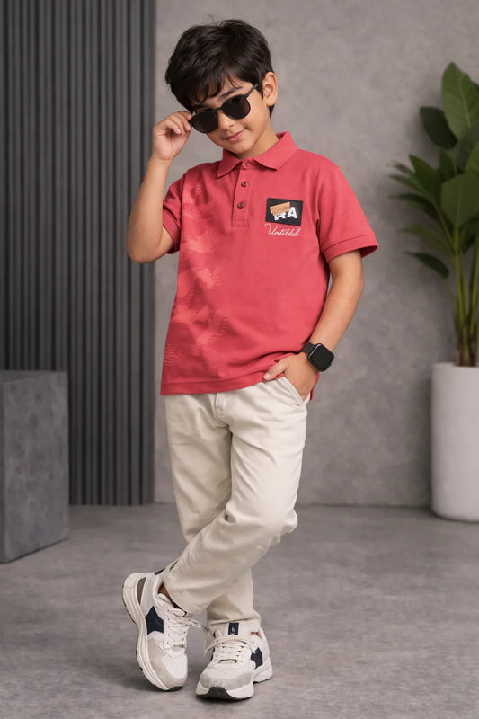 Stylish boy in red polo shirt, beige pants, white sneakers, and sunglasses posing indoors