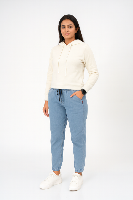 Woman wearing a cream hoodie and light blue jogger pants on a white background
