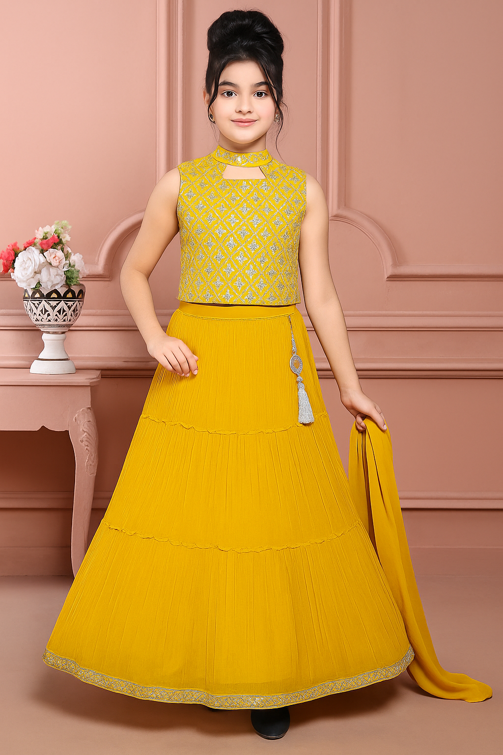 Young girl in a yellow traditional outfit standing against a pink wall.