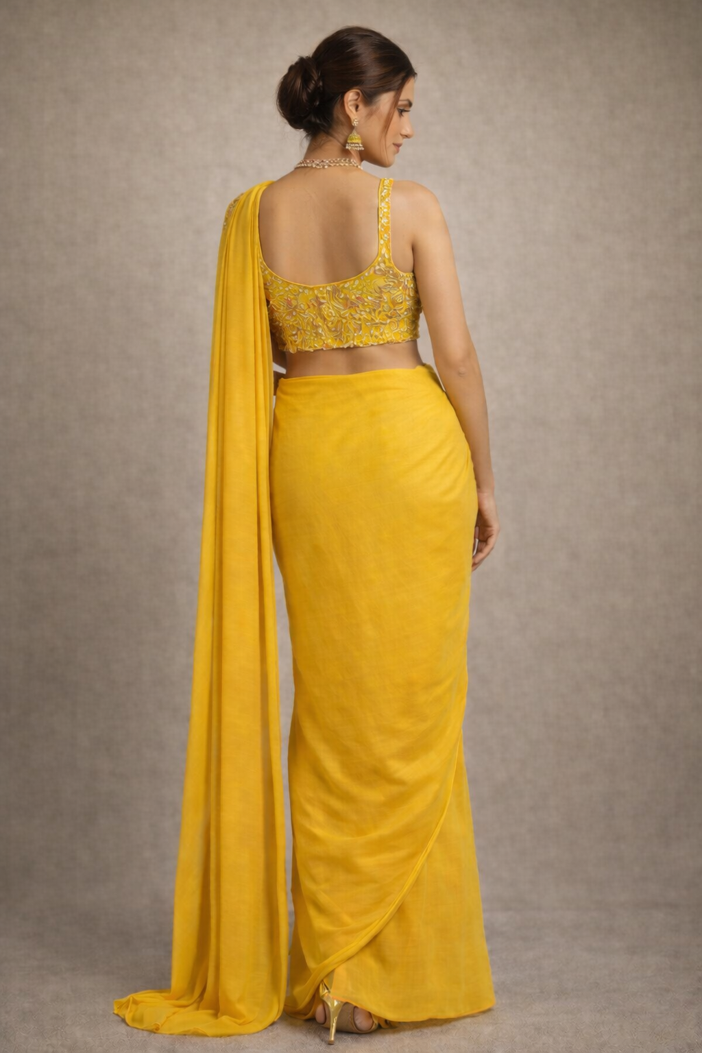 Woman wearing a yellow saree with a plain background