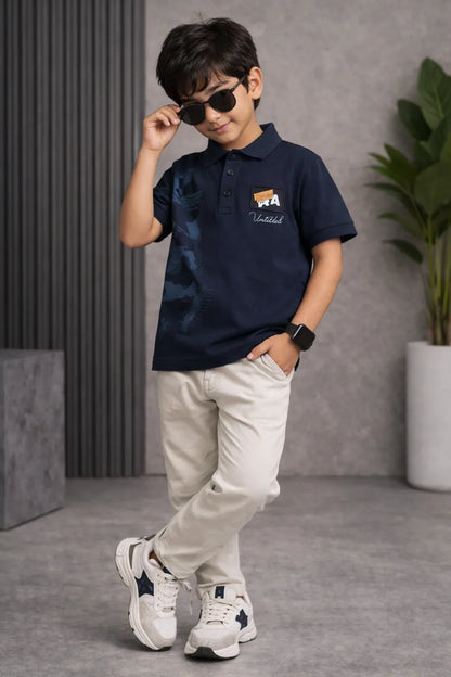 Stylish boy in navy polo shirt, beige pants, sneakers, and sunglasses posing indoors