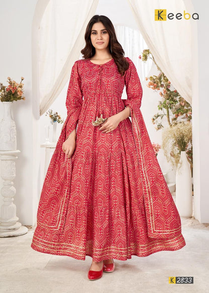 Woman in a red printed ethnic dress with gold detailing, posing indoors with floral decor.